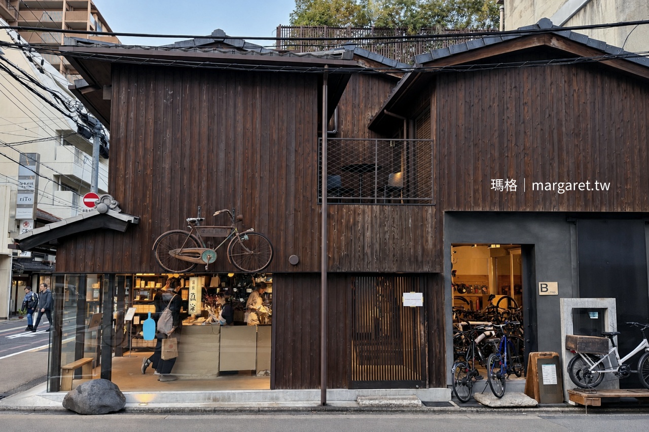 京都 Blue Bottle Coffee 六角店町家外觀，深色木板牆上掛著復古自行車，一樓玻璃窗內是明亮咖啡吧與自行車店