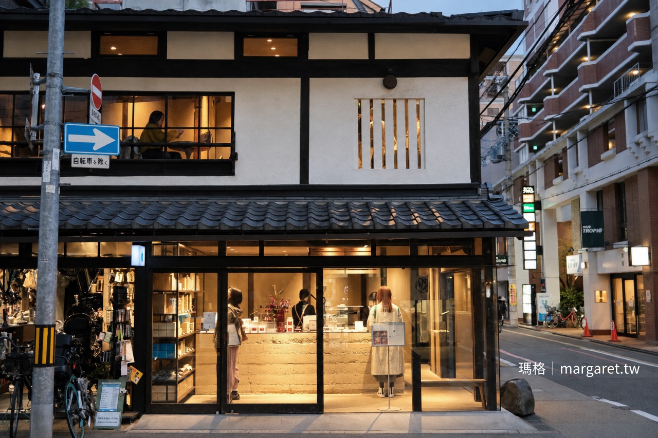 京都 Blue Bottle Coffee 六角店町家外觀，深色木板牆上掛著復古自行車，暮色中一樓玻璃窗透出暖黃燈光
