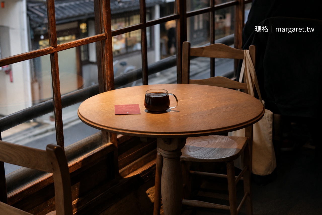 京都 Blue Bottle Coffee 六角店二樓木格窗邊圓桌，桌上放著一杯黑咖啡，窗外可見京都街道景色