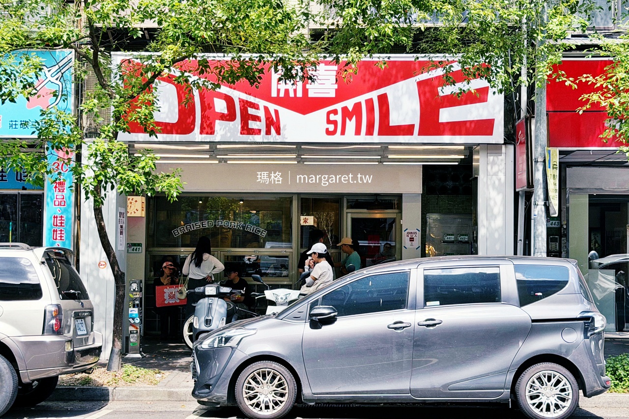 台北信義區莊敬路上的開囍滷肉專賣店，紅白色 OPEN SMILE 招牌被綠樹環繞，店門口有候位客人與停放的汽車